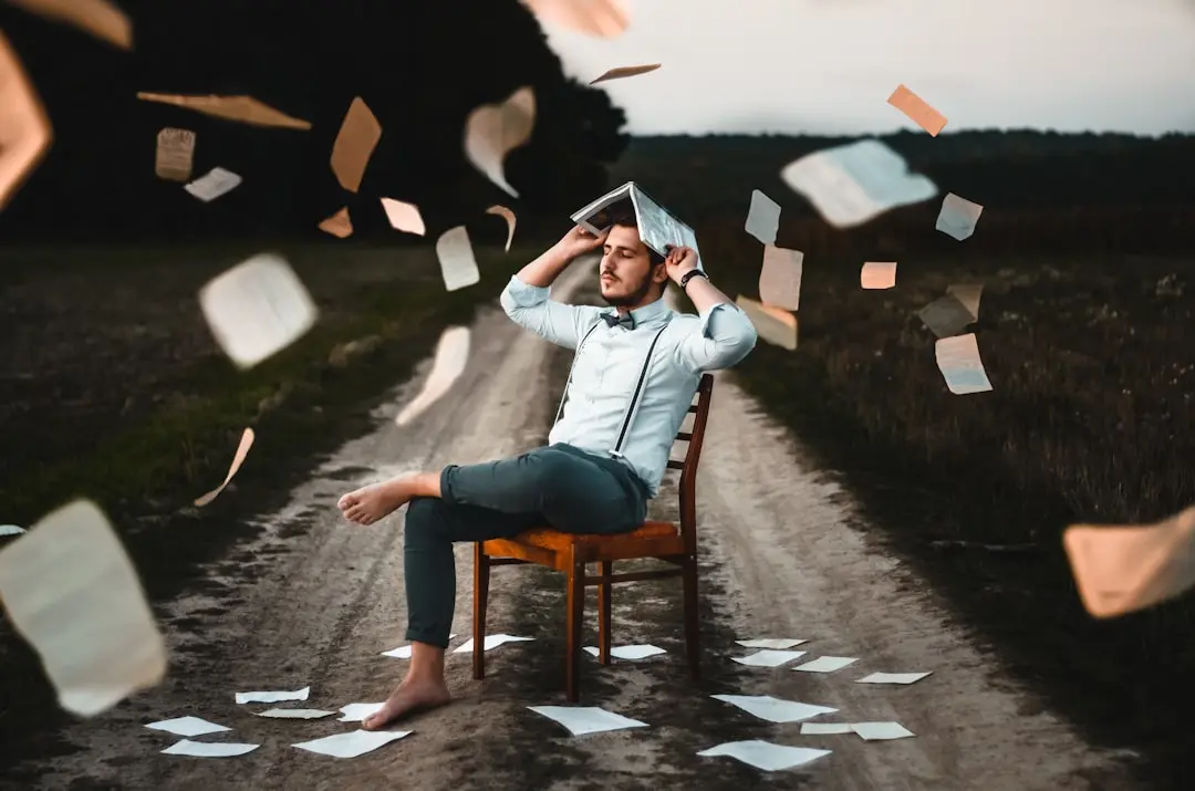 A man sits on a chair in a rural path with papers scattered and flying around him, symbolizing the creativity and challenge in storytelling for interviews.